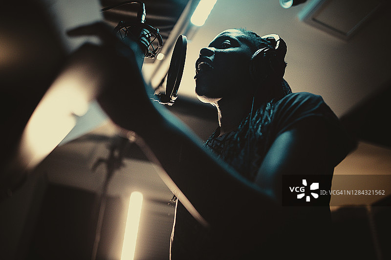 一位年轻漂亮的非裔美国女歌手在专业录音棚录制歌曲。图片素材