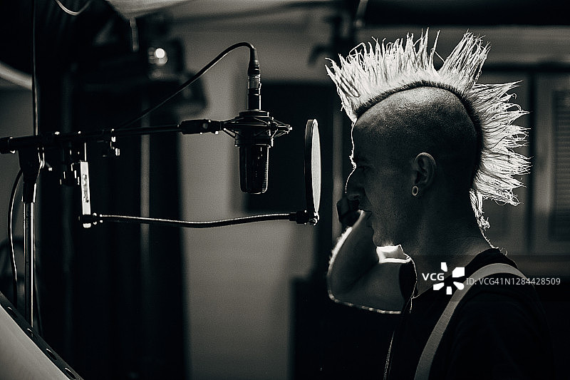 在录音棚里对着麦克风唱歌的朋克男人图片素材