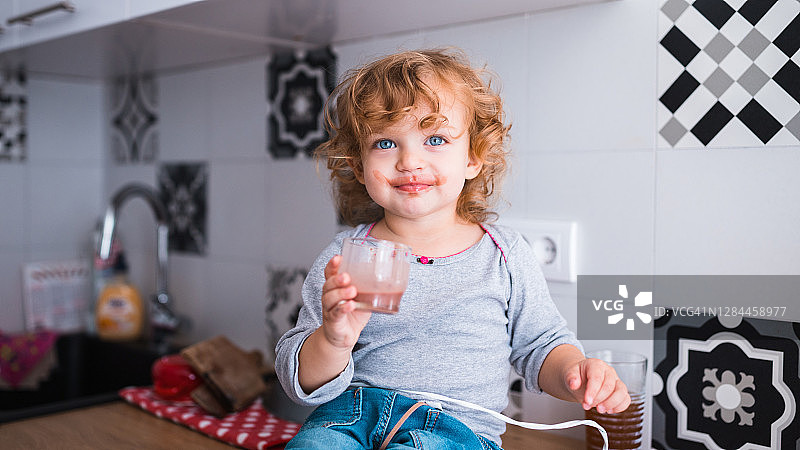 快乐的孩子手拿一杯婴儿食品，吃得一塌糊涂图片素材