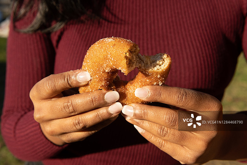 30多岁的亚洲女性拿着一个咬了一口的苹果甜甜圈图片素材