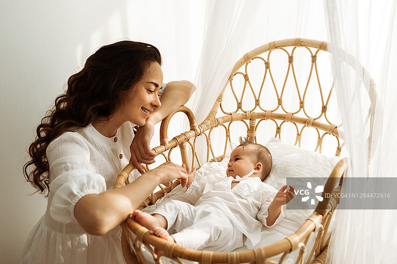 美丽的白人母亲在藤制婴儿床抚摸婴儿图片素材