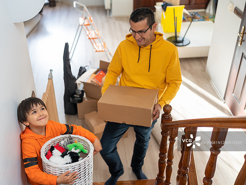 搬家日，可爱的儿子和快乐的父亲抬着盒子走上新家的楼梯图片素材
