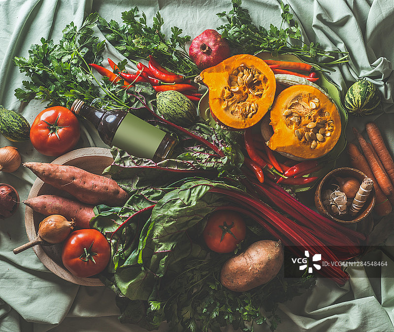 各种秋季时令蔬菜：南瓜、甜菜、洋葱、西红柿、甘薯、绿色调味品、南瓜和橄榄油瓶图片素材