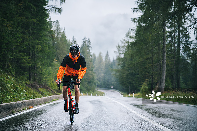 骑自行车的人在雨中沿着湿路骑行图片素材