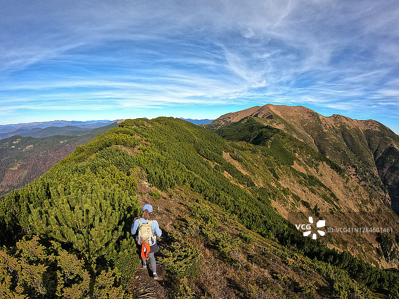 徒步年轻女性背着背包登上山顶，山地景观背景图片素材