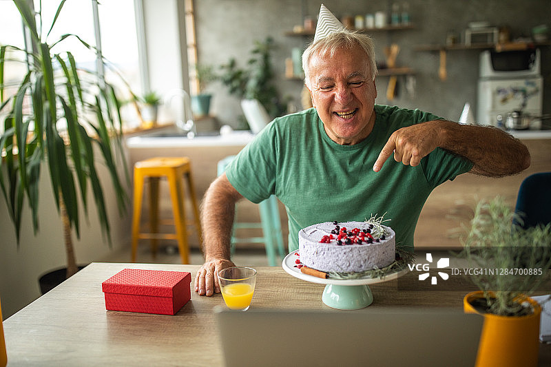 疫情隔离期间，年长的男人独自在家庆祝生日并进行视频通话图片素材