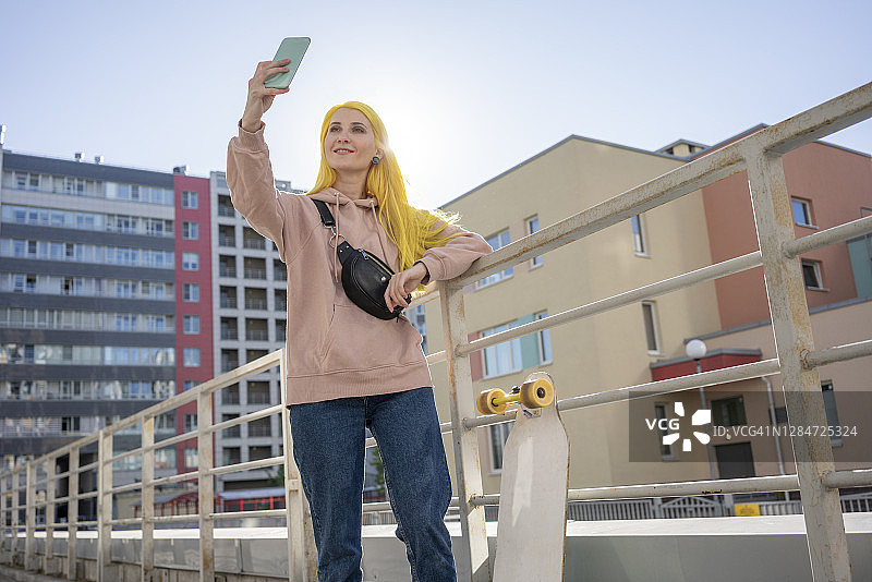 在阳光明媚的日子里用智能手机自拍的微笑年轻女子图片素材