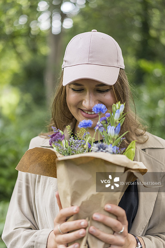 年轻女子在公园里手捧鲜花微笑图片素材