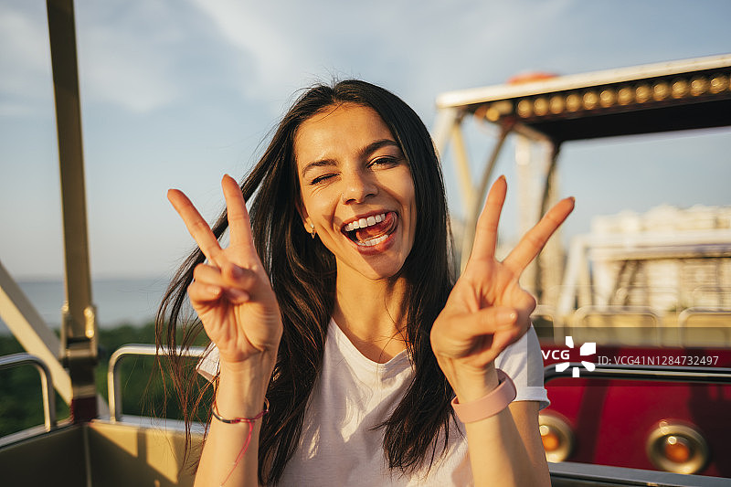 笑容灿烂的女子乘坐摩天轮，比出和平手势图片素材