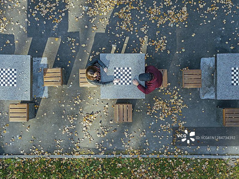 秋天，男朋友在公园的桌旁和女朋友下棋图片素材