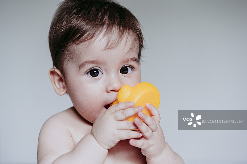 坐在家里把玩具放进嘴里的可爱小男孩图片素材