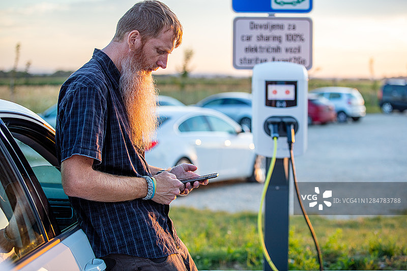男人在停车场使用手机为电动汽车充电图片素材