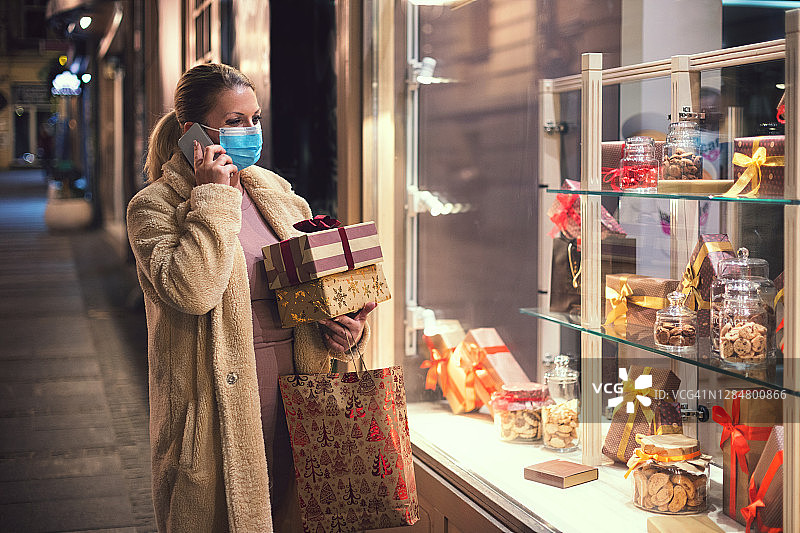 疫情期间，女人戴着防护口罩购买圣诞礼物时讲手机图片素材