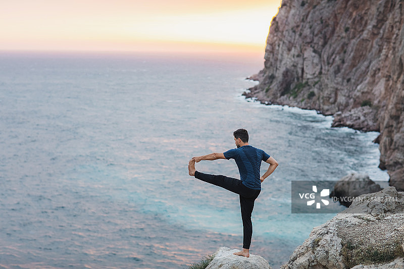 男人在悬崖上做瑜伽，欣赏美丽的海景和山景图片素材
