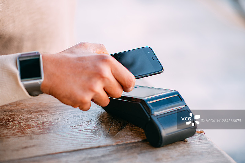 顾客在咖啡馆使用智能手机进行NFC支付图片素材