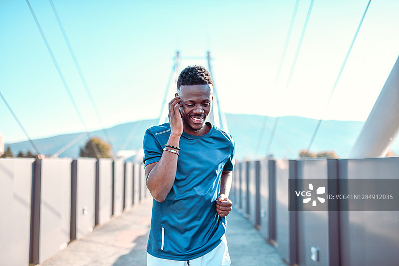 在桥上跑步时用智能手机交谈的非洲男子图片素材
