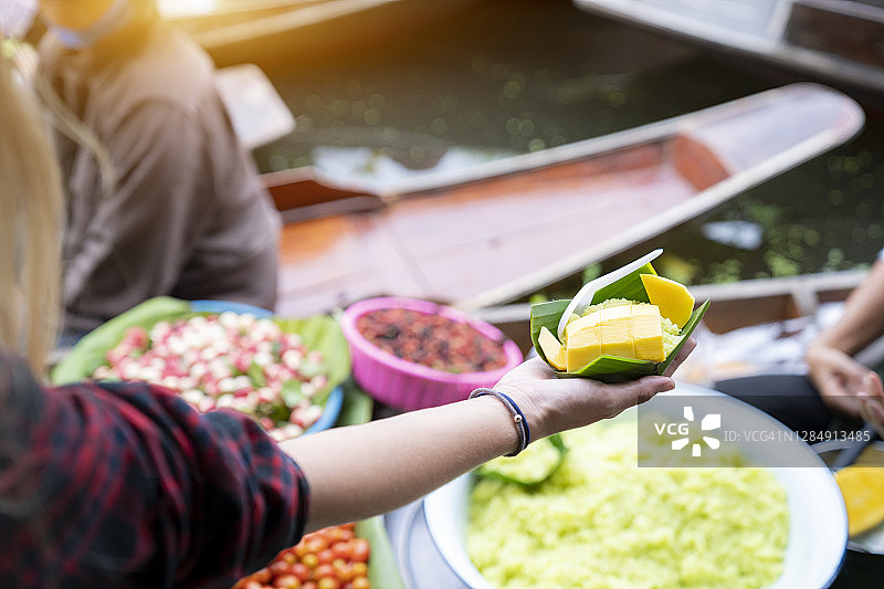 在泰国水上市场，游客从女商人那里收到芒果糯米饭图片素材