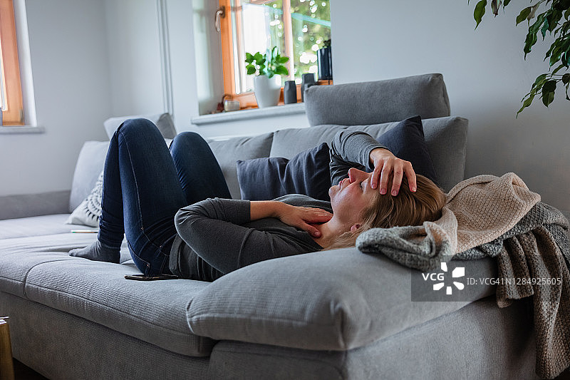 头痛的生病女人躺在沙发上图片素材