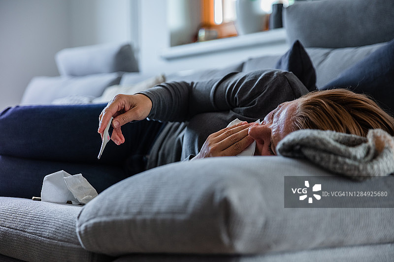 在家躺在沙发上看体温计的生病女人图片素材