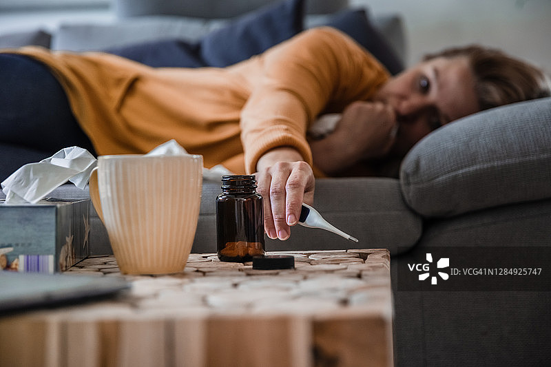 生病的女人在家里沙发上看温度计图片素材