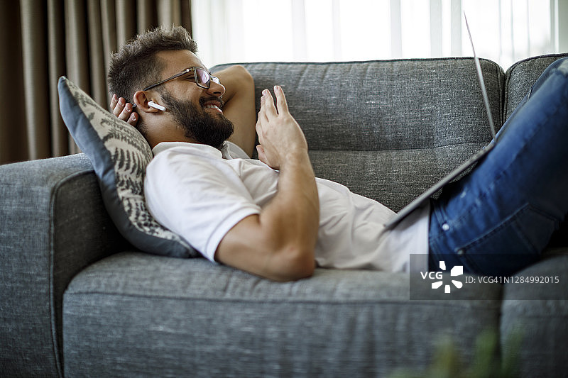戴无线耳机进行视频通话的年轻微笑男人图片素材