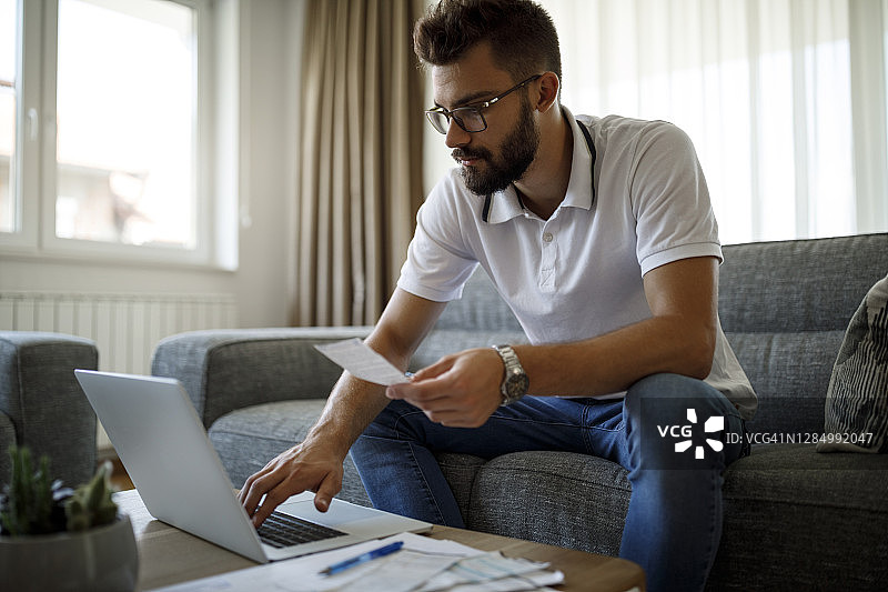 年轻男人在家用笔记本电脑支付账单图片素材