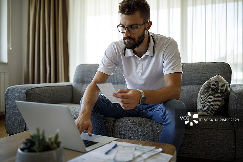 年轻男人在家用笔记本电脑支付账单图片素材