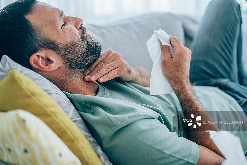 年轻男子喉咙痛躺在沙发上图片素材