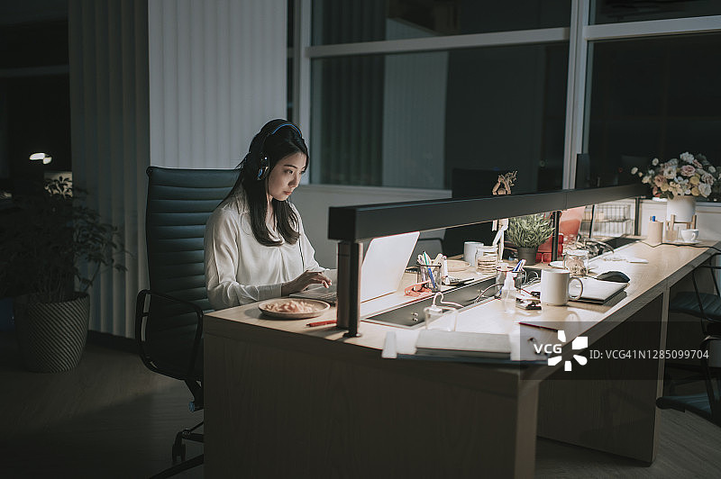中国女白领在呼叫中心加班，戴着耳机与海外客户交谈图片素材