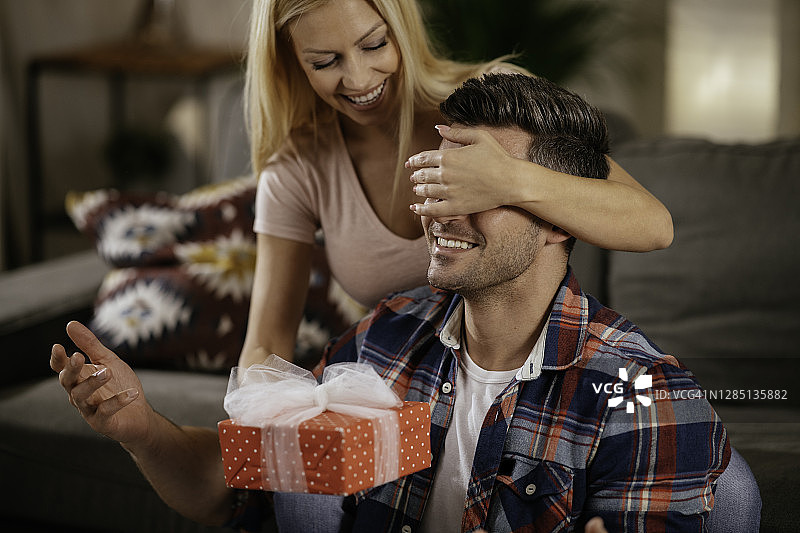 迷人的女孩闭上丈夫的眼睛，拿着给他的礼物图片素材