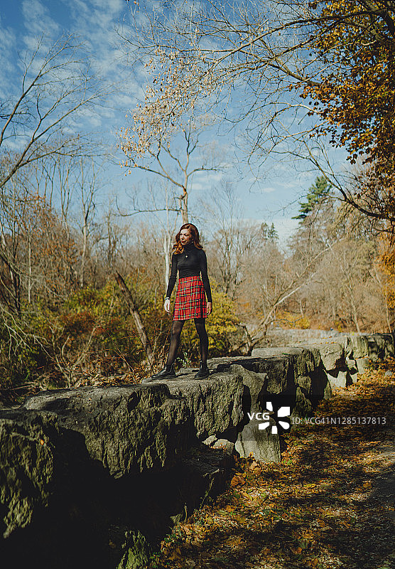 年轻女子身穿高领毛衣和红色短裙站在岩石上图片素材