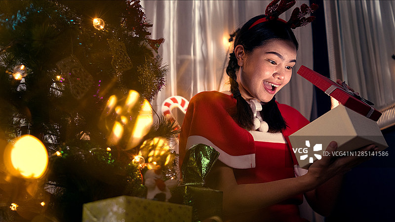 亚洲女人穿着圣诞老人服装，在屋里靠窗的客厅里装饰圣诞树图片素材