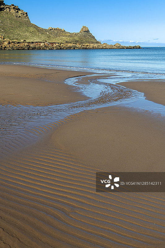 小溪引导视线穿过波纹海滩沙滩，到达倾倒的烟囱岩堆图片素材