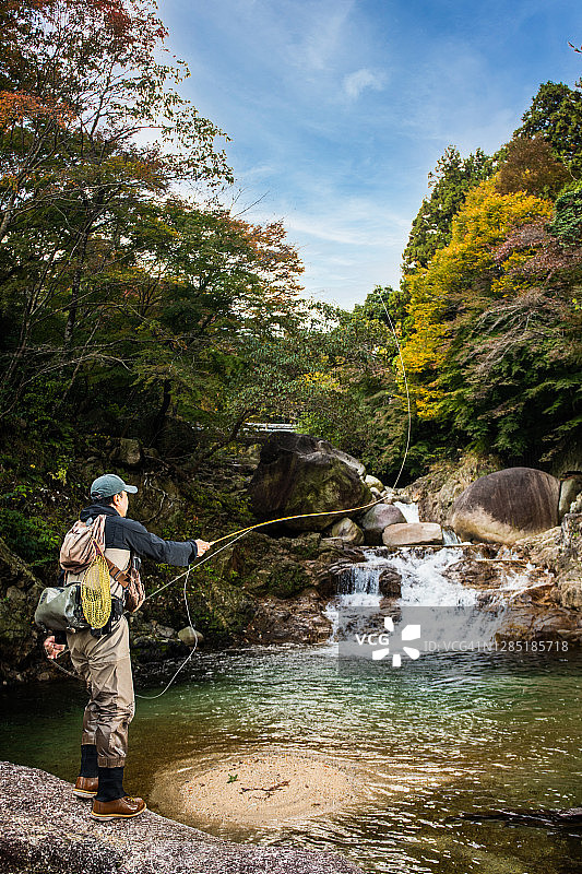 男子在有瀑布的山间河流中飞蝇钓鱼图片素材