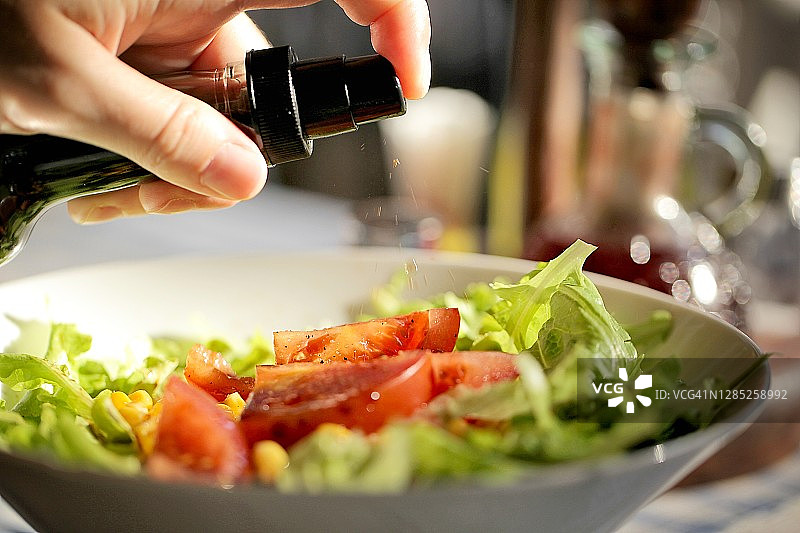 从上方直接拍摄的手在碗里的绿色沙拉上喷洒香醋图片素材
