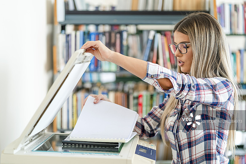 在图书馆使用复印机的可爱金发女子图片素材