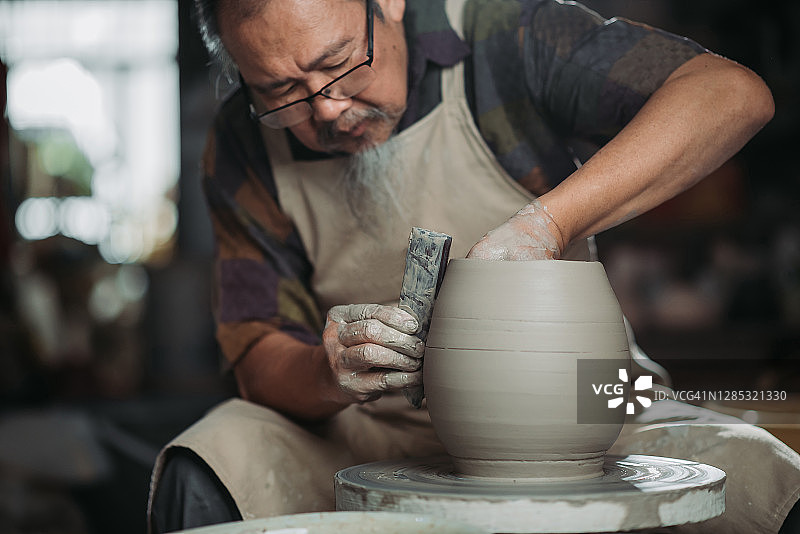 年长的华人陶艺家在工作室用陶轮制作陶器图片素材