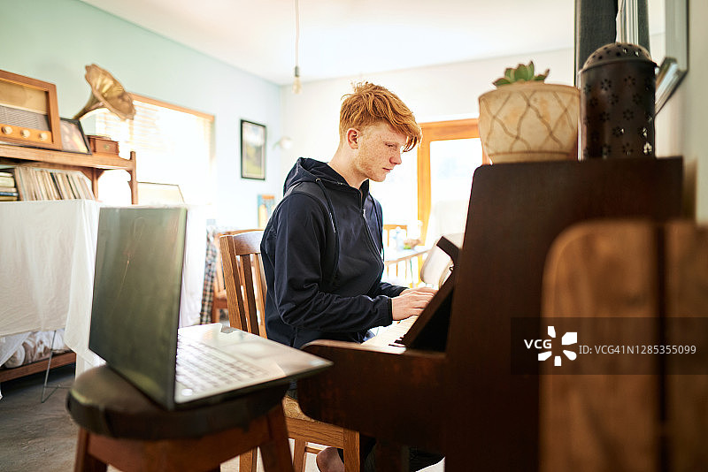 男孩用笔记本电脑上网课并弹钢琴图片素材