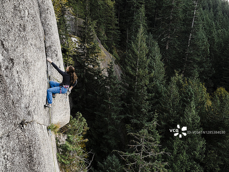 运动型女性攀岩者攀登不列颠哥伦比亚省斯阔米什附近沿海雨林上方的大岩壁图片素材