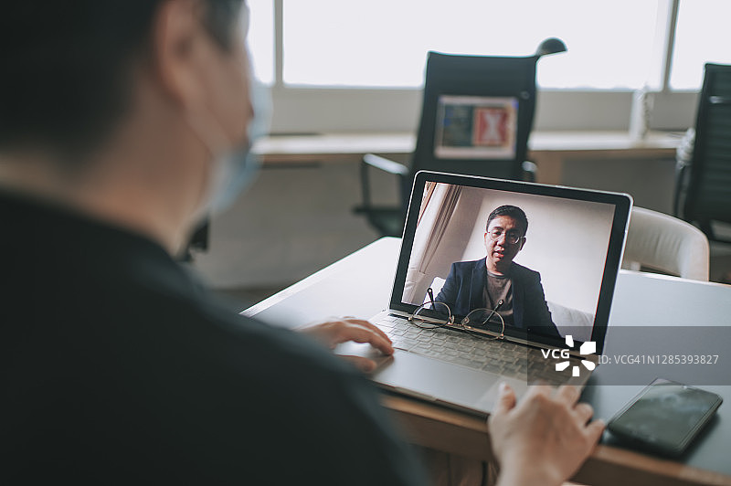 中国女性在共享办公场所佩戴口罩，保持社交距离并使用笔记本电脑进行视频通话图片素材