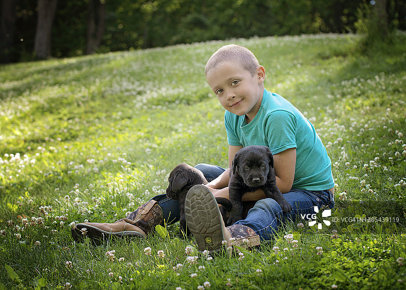 草地上抱着黑色拉布拉多幼犬的男孩图片素材