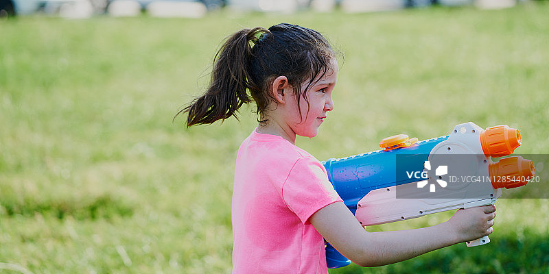 女孩在花园里穿着粉色T恤玩水枪图片素材