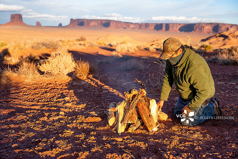一位美洲原住民纳瓦霍族男子整理木柴准备生火取暖，背景是纪念碑谷的标志性纪念碑图片素材