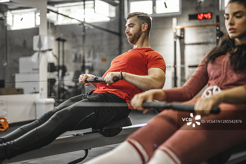 年轻情侣在健身俱乐部使用划船机图片素材