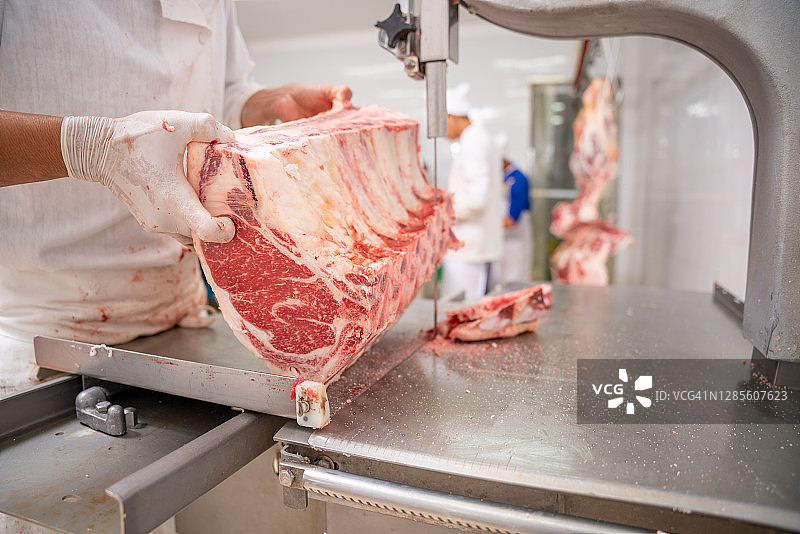 肉店工人用电动带式切割机在屠宰场切割肉块特写，肉类行业，和牛图片素材