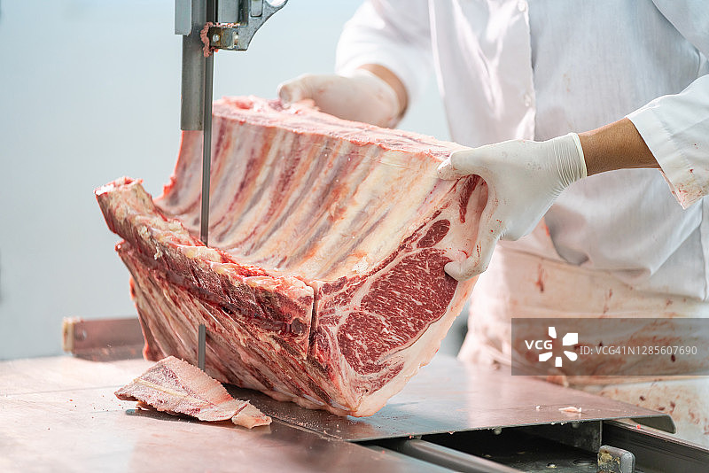 肉店工人用电动带式切割机在屠宰场切割肉块特写，肉类行业，和牛图片素材