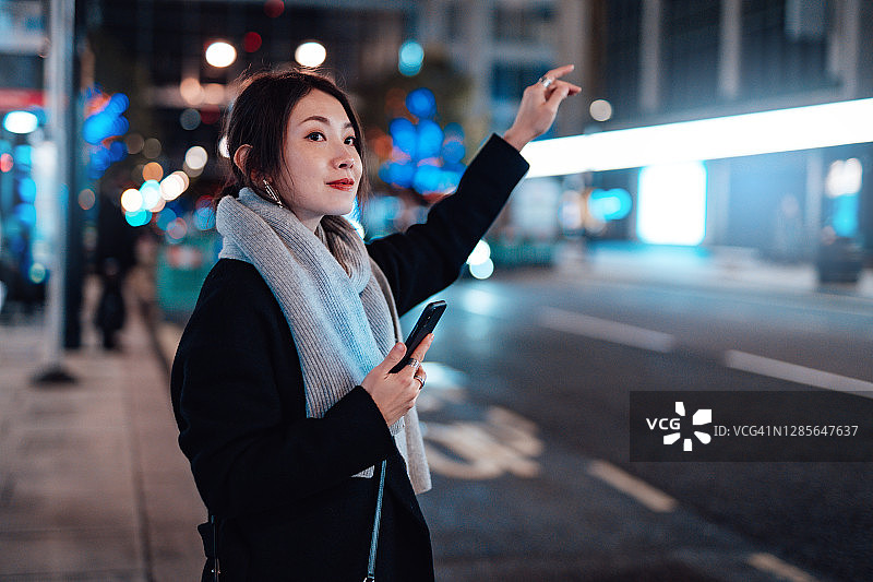 在夜晚的城市里用智能手机叫出租车的年轻女人图片素材