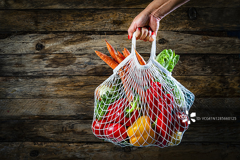 女人手拿装满新鲜有机蔬菜的网状购物袋。复制空间图片素材