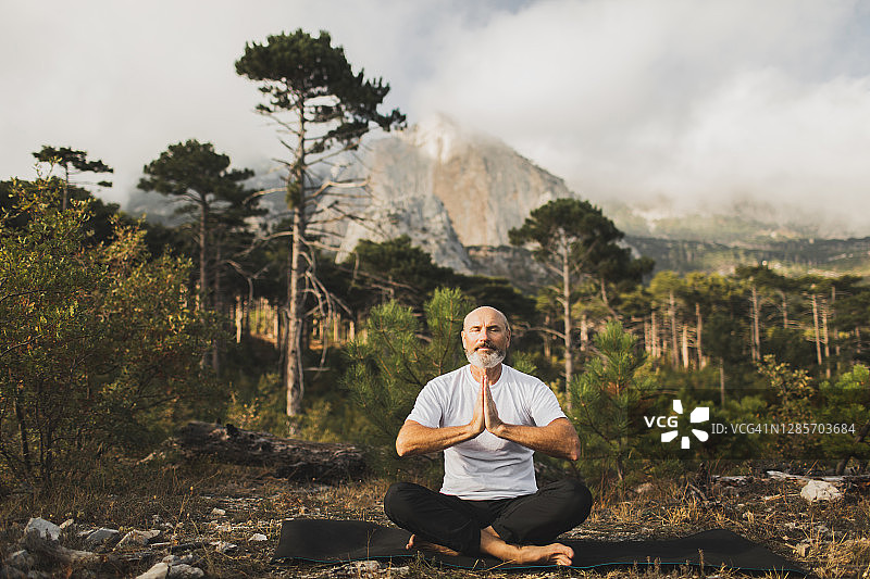 男性老年人在户外练习瑜伽，欣赏山景。独自祈祷和冥想，追求健康与自然和谐。图片素材