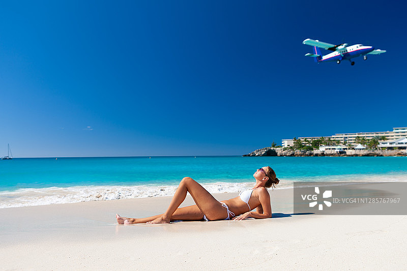 在热带海滩海岸线上放松，飞机飞过的女人图片素材